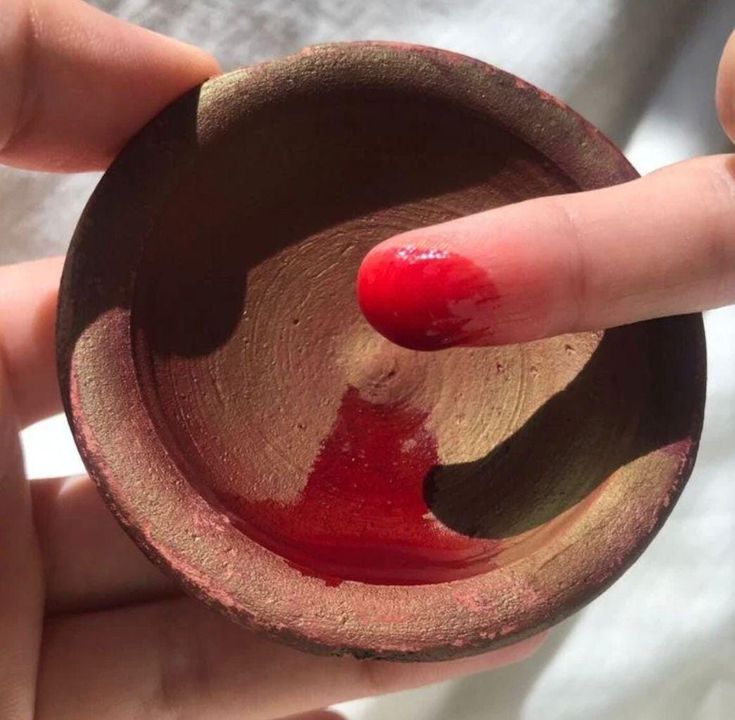 Mirath Beauty Aker Fassi in a traditional clay pot, showing the natural red tint on the finger from Moroccan poppy flowers and pomegranate rind blend.