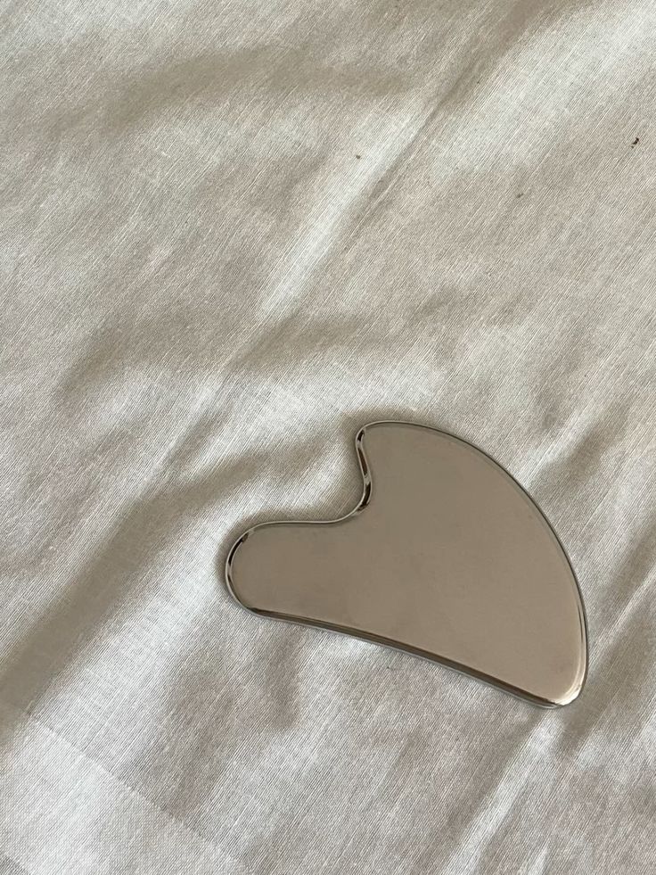 Stainless steel gua sha facial tool on linen fabric - luxury skincare ritual for sculpting, lifting, and ymphatic drainage by Mirath Beauty, in Lebanon